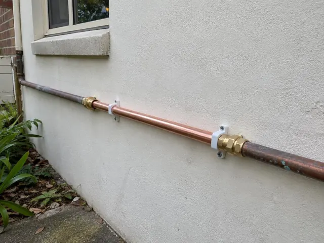 Copper water pipe repair on an exterior rendered wall beside a window in Argenton