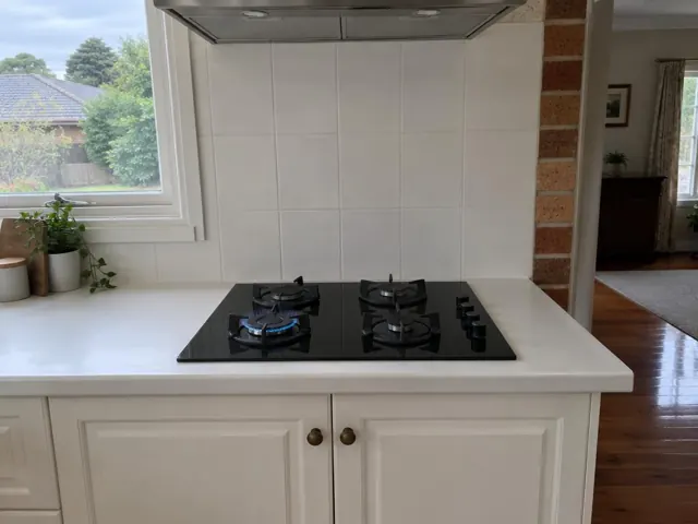 Black gas cooktop set into a white benchtop with tiled splashback and window in West Wallsend