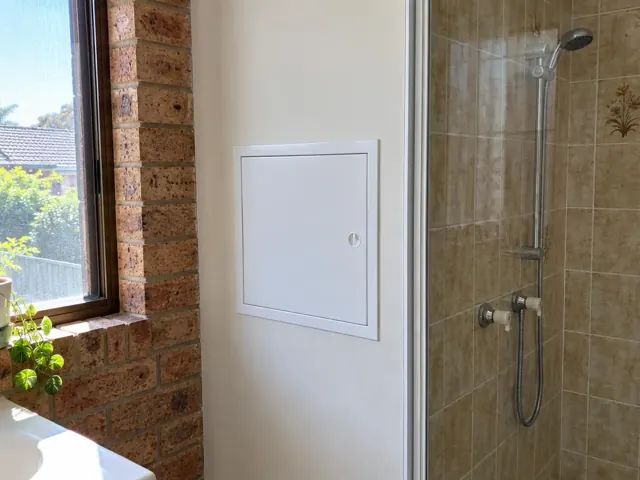 Bathroom wall with a small access panel beside a tiled shower in Elermore Vale