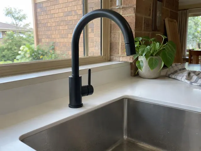 Matte black kitchen mixer tap beside a stainless sink on a light benchtop near a brick window in Edgeworth